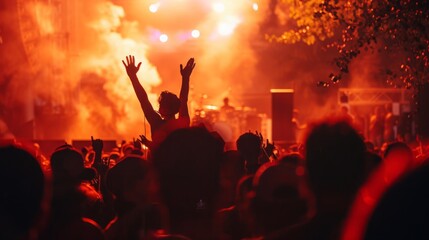 A large group of individuals at a live music event, energetically cheering with their arms lifted high in the air.