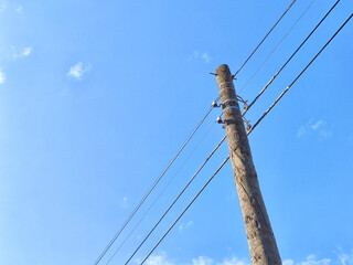 Old power line pole against blue sky in sunny day