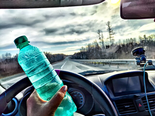 Driver Holding Water Bottle During Road Trip. Hand holding a water bottle in car with view of road....