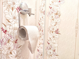 Toilet paper on a chrome holder against decorative floral wallpaper. Restroom Toilet Paper Holder With Floral Wallpaper
