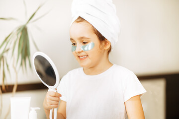 Funny little girl with towel on her head with eye mask looking in a mirror. Spa, healthcare,...