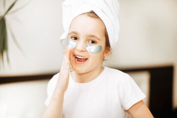 Funny little girl with towel on her head looking at camera with eye mask. Spa, healthcare, morning...