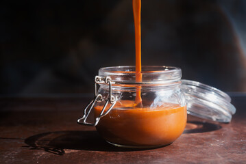 Homemade caramel sauce pouring on a glass jar