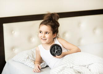 Cute little kid girl lying on bed waking up in morning stopping alarm clock