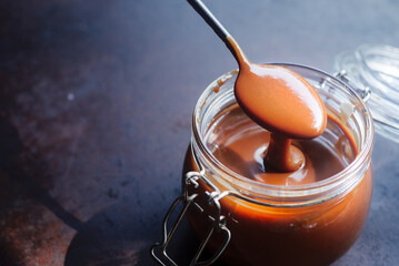 Homemade caramel sauce on spoon dripping down to a glass jar