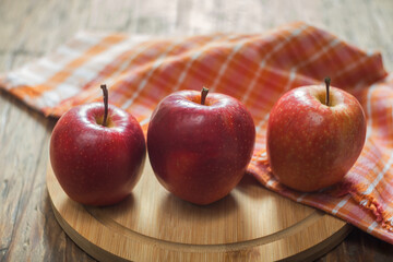 Three red apples on a wooden board with a checkered tablecloth