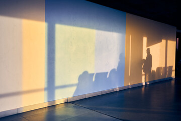 A silhouette of a man on a stone wall at the airport with space to copy. Shadows of people and chairs. Yellow and blue shades of light on the wall. High quality photo