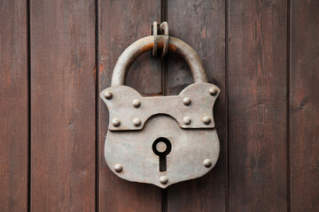 Old rusty padlock on a wooden door.   Wooden Gate With Large Hinged Iron Lock In The Village