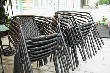  Stacked chairs near cafe tables standing on street . Closed outdoor cafe .