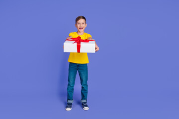 Photo of positive cheerful cute nice boy wear trendy yellow clothes hold big gift celebrate holiday isolated on violet color background