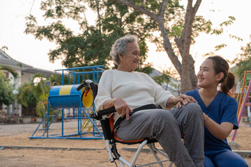 Young nurse and elderly asian senior woman on wheelchair, Asian careful caregiver and patient,  Nurse gives a pep talk to an elderly female patient in the garden in the evening. Health insurance.