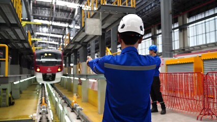 Electric Train Maintenance Training Center, male maintenance technicians wearing a uniform and helmet  standing  hand signal  tracks  electric train in the electric train maintenance station
