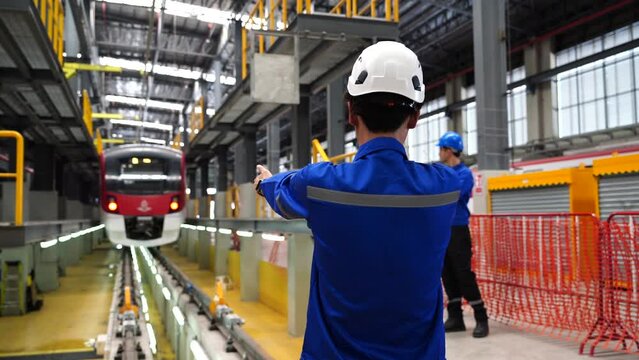 Electric Train Maintenance Training Center, male maintenance technicians wearing a uniform and helmet  standing  hand signal  tracks  electric train in the electric train maintenance station