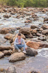 lifestyle. young indian sitting on the rocks next to the rapids of the river