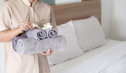 Hands of hotel maid putting plumeria flower and towels on the bed in the luxury hotel room ready...