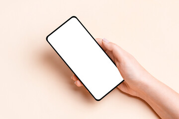 Female hand holding a phone with a blank screen on a beige background
