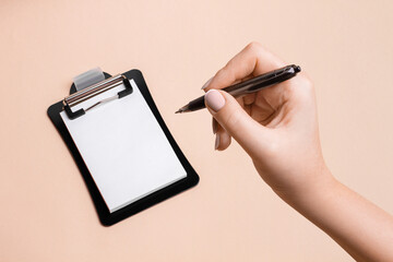 White paper on a black plate and a woman's hand about to write on a beige background