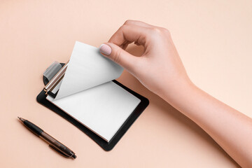 A woman's hand flips through pieces of paper for notes on a beige background.