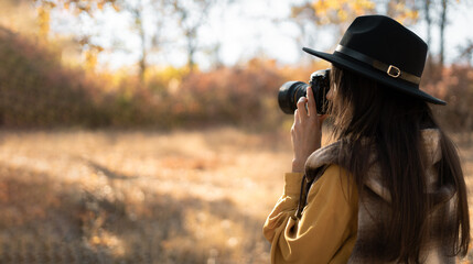 Woman photographer in a hat photographing autumn nature. Travel and hobby concept
