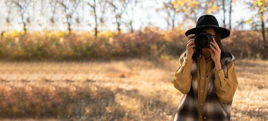 Portrait of female tourist photographer taking photo of autumn forest. Travel and hobby concept....