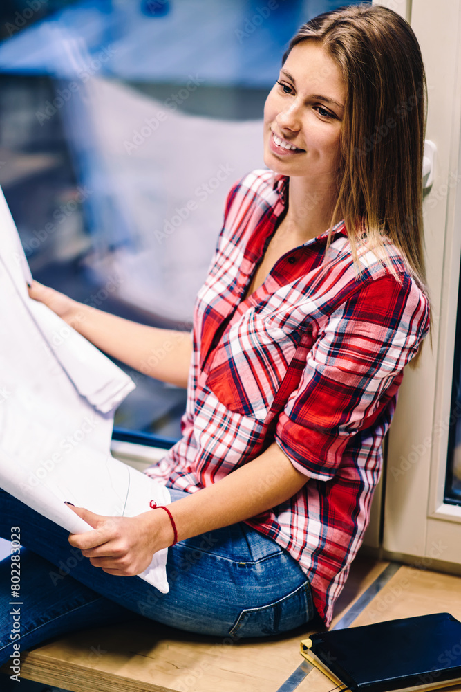 Poster smiling woman holding papers with drawings satisfied with completing blueprint before deadline sitti