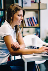 Smiling hipster girl satisfied with useful online language courses watching videos for learning via...