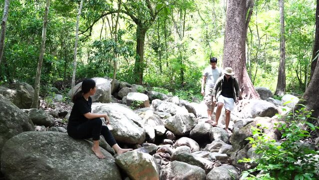 Group of three Asian friends, two men and one woman, have a good relationship, hiken rock climbing at the waterfall stream in the forest is happy summer time trip during the vacation.Lifestyle concept
