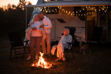 The family is relaxing together by the campfire near their mobile home. Evening family vacation