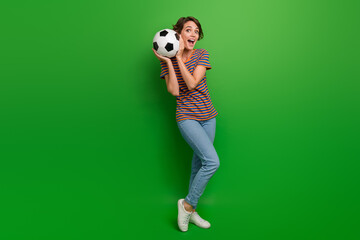 Full size portrait of funky cheerful astonished girl arms hold football isolated on green color background