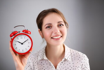 Adult smiling caucasian woman hold red alarm clock on gray background. - obrazy, fototapety, plakaty