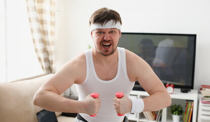 Young attractive man engaged in fitness at home holding dumbbell in hand trying to fight excess weight and loss - obrazy, fototapety, plakaty