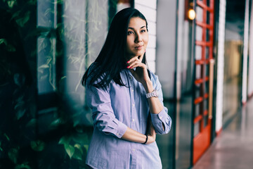 Obraz premium Charming positive pensive brunette woman dressed in stylish clothes dreaming about successful business startup indoors.Gorgeous contemplative hipster girl pondering while standing in modern office