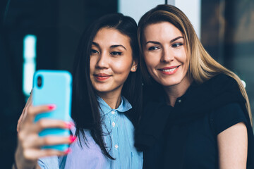 Beautiful successful female best friends dressed in trendy outfit making selfie on smartphone camera for sharing in social networks.Cute positive hipster girls having fun while taking picture