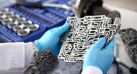 The auto repair service repairman in automatic gearboxes holds in his hand in blue protective gloves the hydroblock detail dehydrates the diagnostics and estimates the detail test transmission closeup