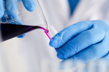 Male chemist holds test tube of glass in his hand overflows a liquid solution of potassium permanganate conducts an analysis reaction takes various versions of reagents using chemical manufacturing.