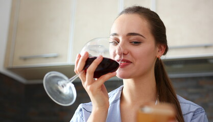 Beautiful smiling brunette woman hold in arms glass of red wine at kitchen table portrait. Vine cabernet merlot sauvignon lips beauty concept - obrazy, fototapety, plakaty