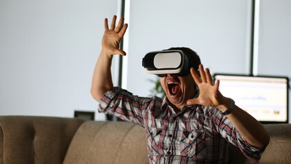 Man sits at home on the couch uses virtual reality glasses rides on a roller coaster screaming in...