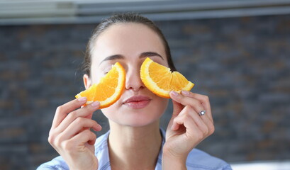 Beautiful brunette smiling woman eat sliced raw tasty orange half at kitchen in the morning...
