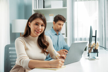 Smiling beautiful woman working on laptop aligning taking note to pose for looking at camera photo...