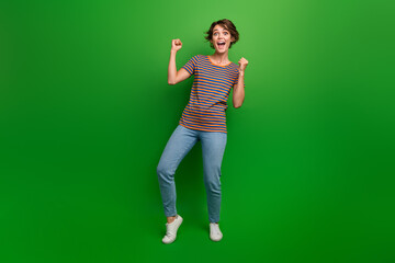 Full size portrait of overjoyed glad girl raise fists shout yeah hooray isolated on green color background