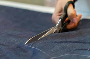 Close up view of hand with scissors cutting a fabric.