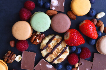 Macarons, chocolate, cookies, berries and various nuts on dark blue background. Top view.
