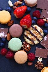 Macarons, chocolate, cookies, berries and various nuts on dark blue background. Top view.