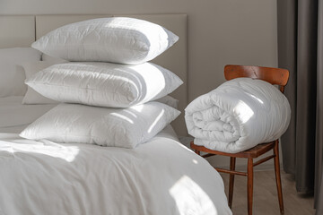 A bed with white pillows and a blanket, next to a bedside table with a lamp, daylight - obrazy, fototapety, plakaty