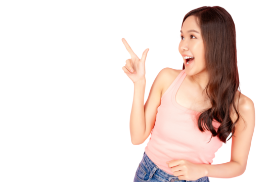 Happy young Asian woman pointing upwards with excitement, isolated on a soft pink background, expressing joy and enthusiasm.
