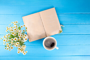 Obraz premium Chamomile daisy flowers bouquet, book, tea or coffee cup, relaxation holiday simple life enjoy summer background, on light blue wood background, top view copy space. Good day, good morning wishing