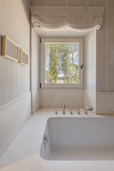 A white porcelain bathtub with marble surrounds with vintage-style faucets and a white aluminum...