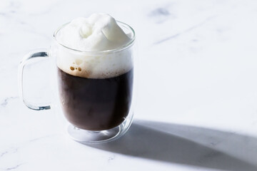 Coffee time - transparent cup of coffee with milk foam at the top. White background