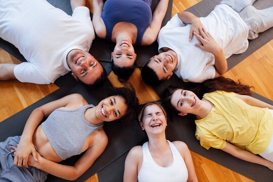 Multi-racial smiling people lie on mats after doing yoga at a fitness club. A group of young athletes relax and rest after physical exercises in the gym.