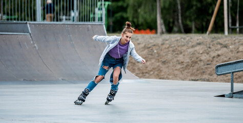 Beautiful girl roller skater riding in city park with ramp. Pretty female teenager rollerskating in...